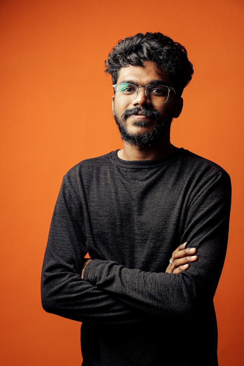 a man with a beard and glasses standing with his arms crossed